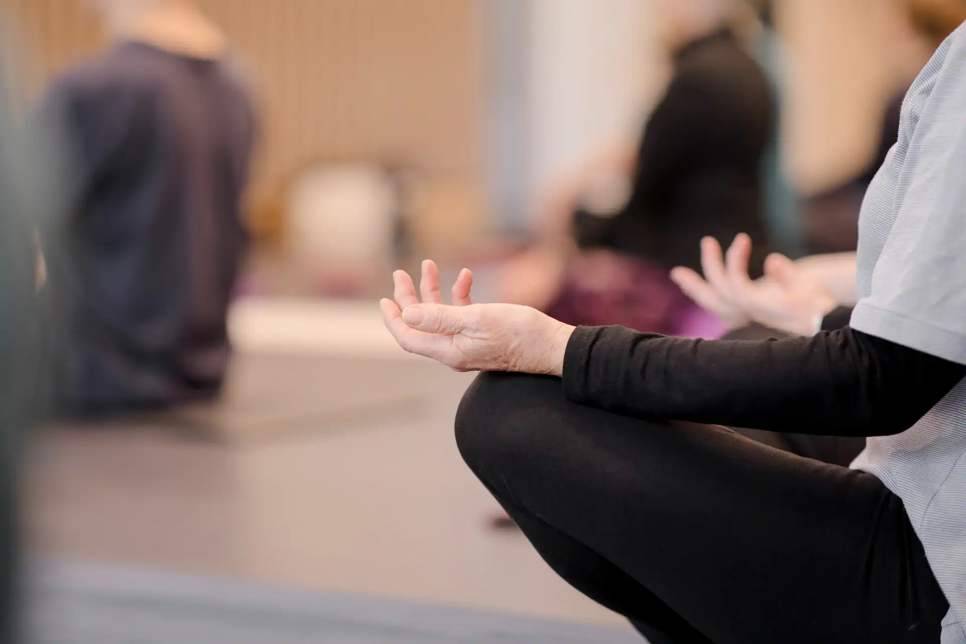 Person meditating in a class, sitting cross-legged with hands in a mudra.