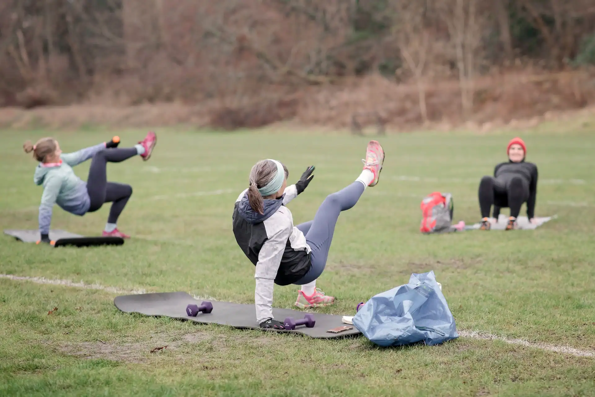 Outdoor Pilates class with women exercising on mats in a grassy field.