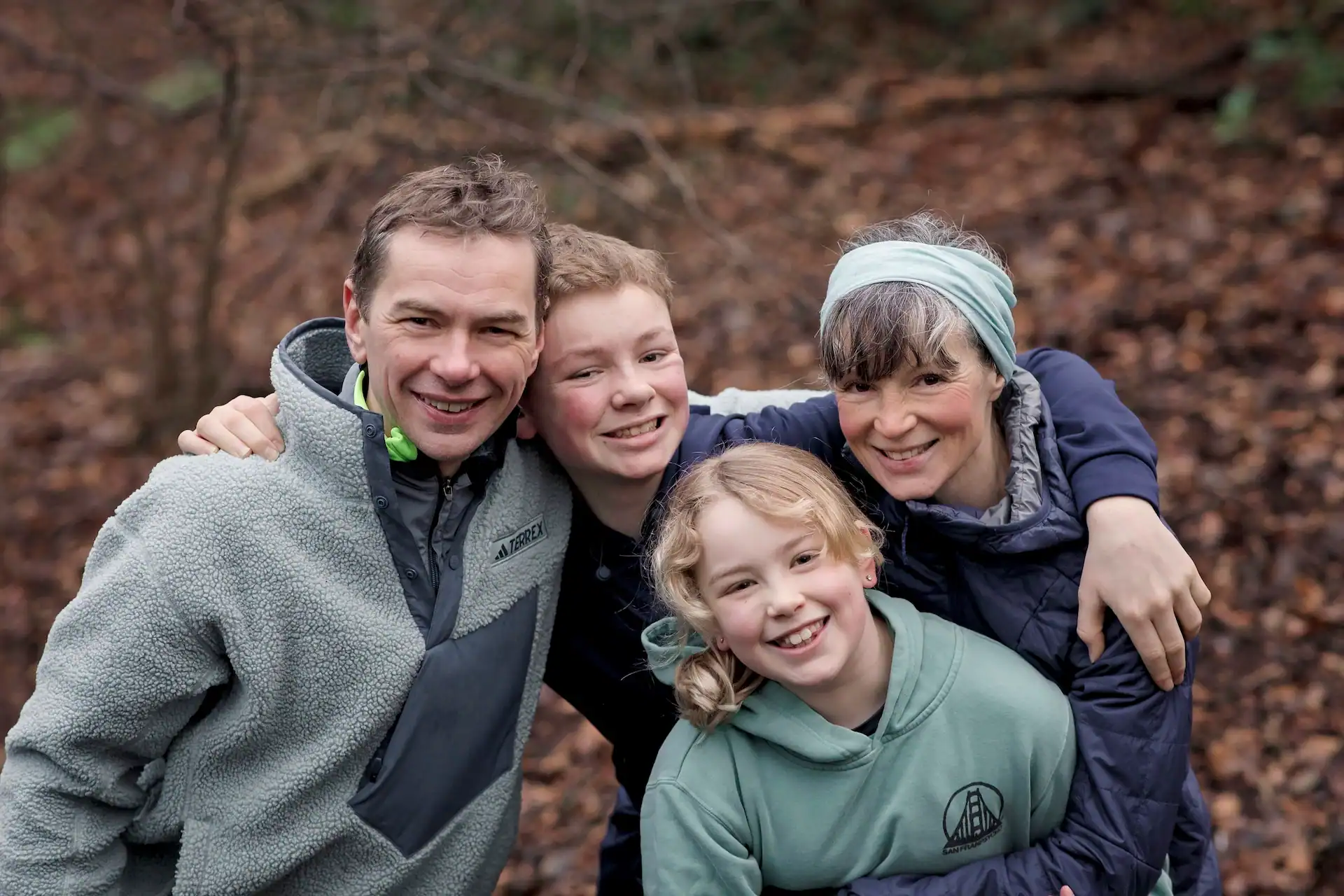 Family outdoor walk in autumn forest, smiling and embracing.